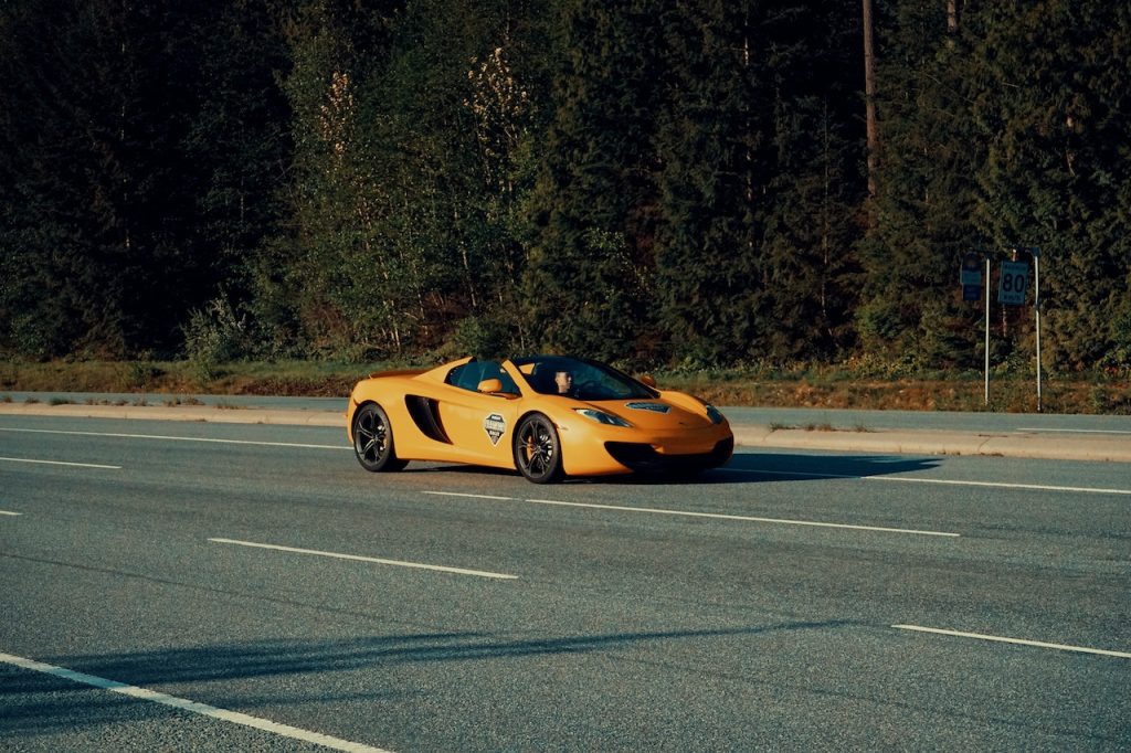 Carro esportivo amarelo em uma estrada, com pinheiros no plano de fundo.