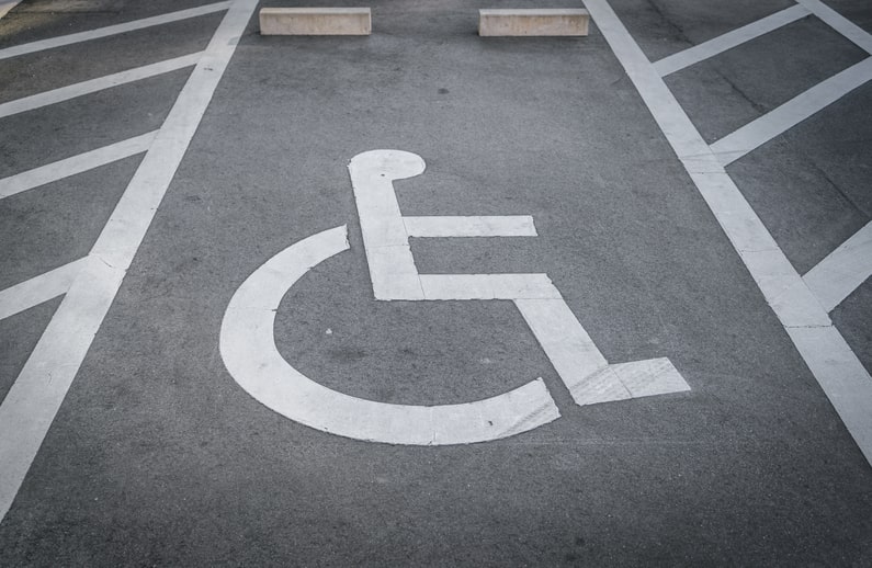 Vaga de estacionamento para pessoas com deficiência. O chão é cinza e a tinta delimitando a vaga é branca.