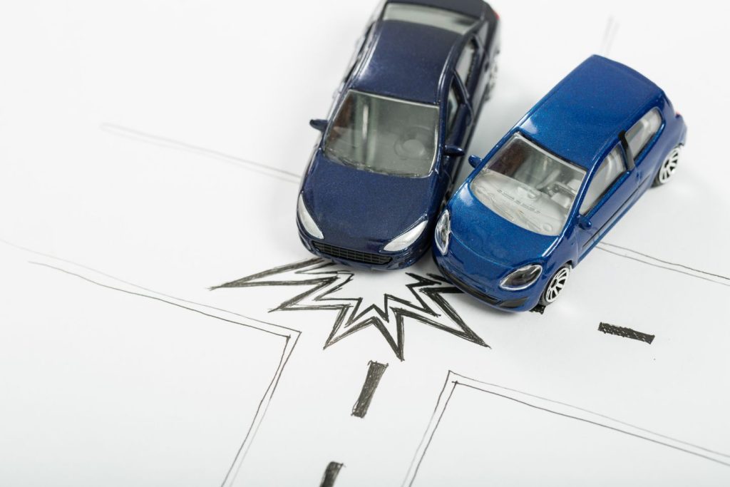 A cobertura para seguro auto certa pode ser de grande ajuda em um acidente, com descrito na imagem. Aqui, dois carrinhos de brinquedo azuis entram em colisão em uma rua feita de papel.
