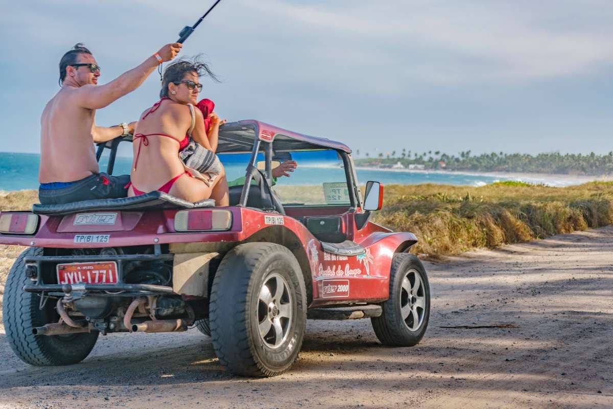 Casal em trajes de banho Jipe vermelho praia e céu azul