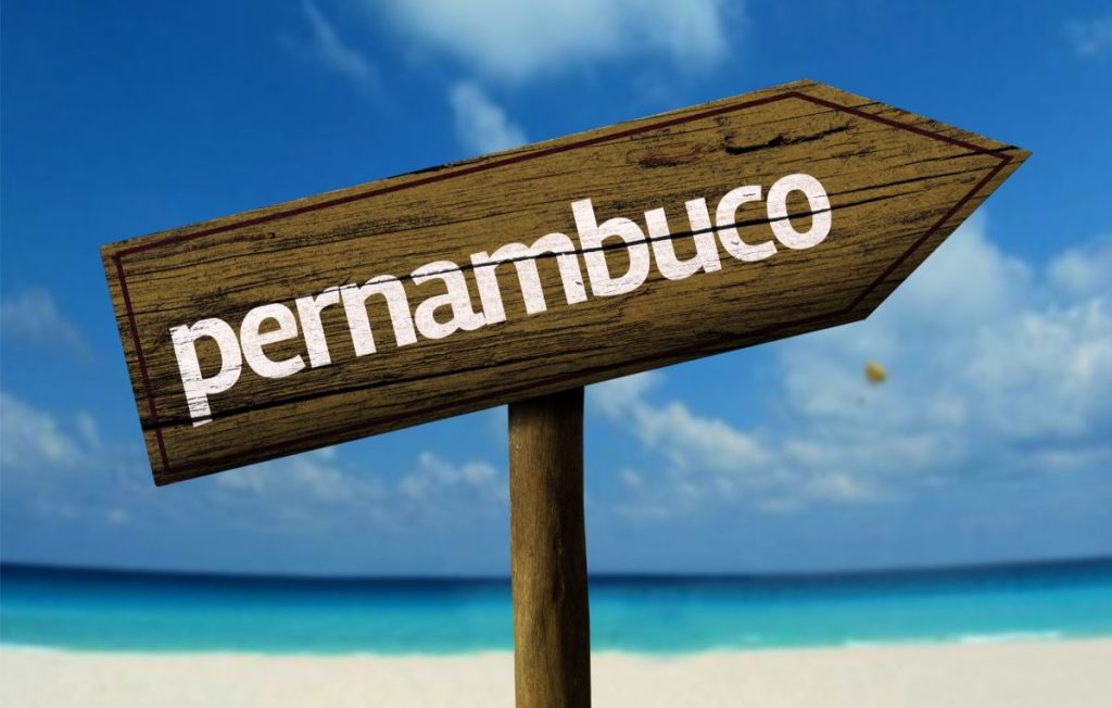 placa de madeira indicando Pernambuco
ao fundo praia e areia branca e céu azul